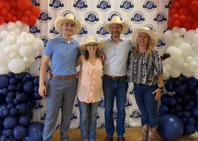 Four team members in cowboy hats and Western attire in front of a BCH 40th anniversary backdrop